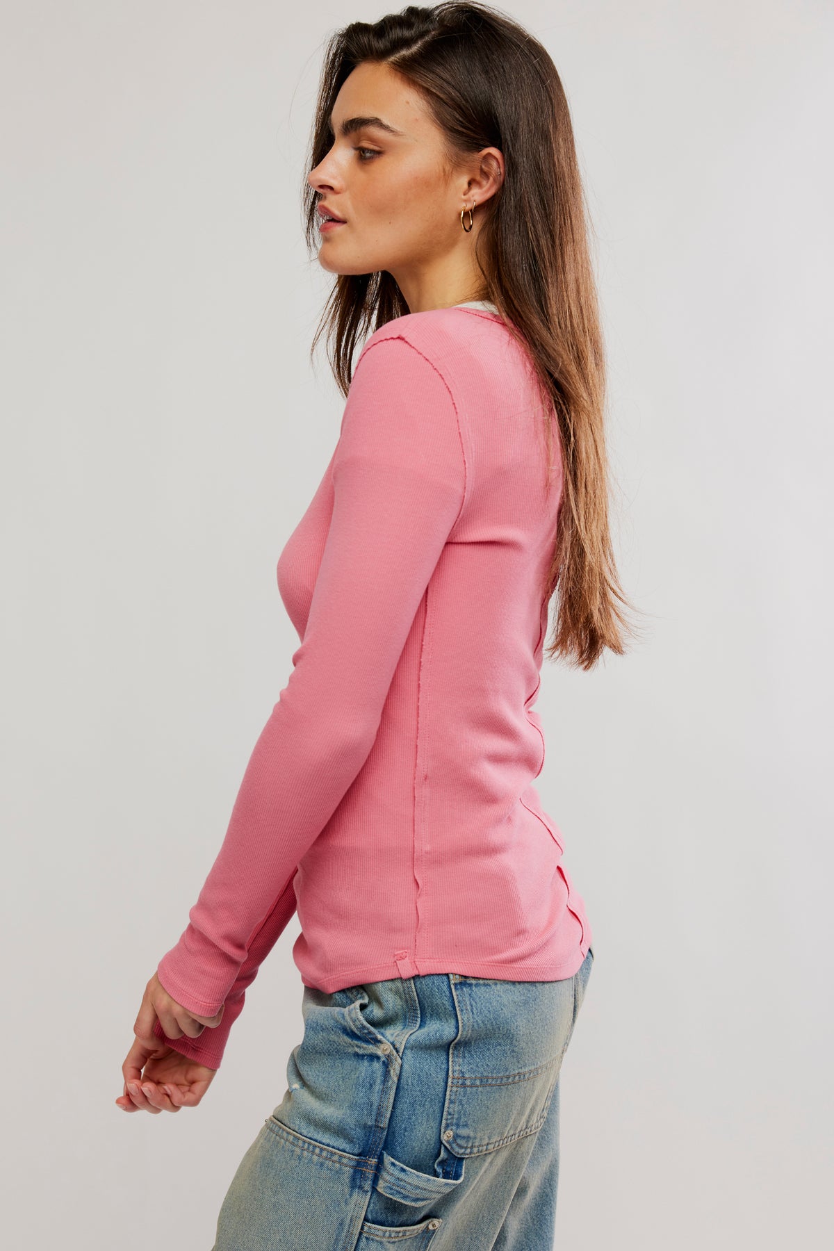 Woman wearing a pink long-sleeve top and blue jeans on a plain background