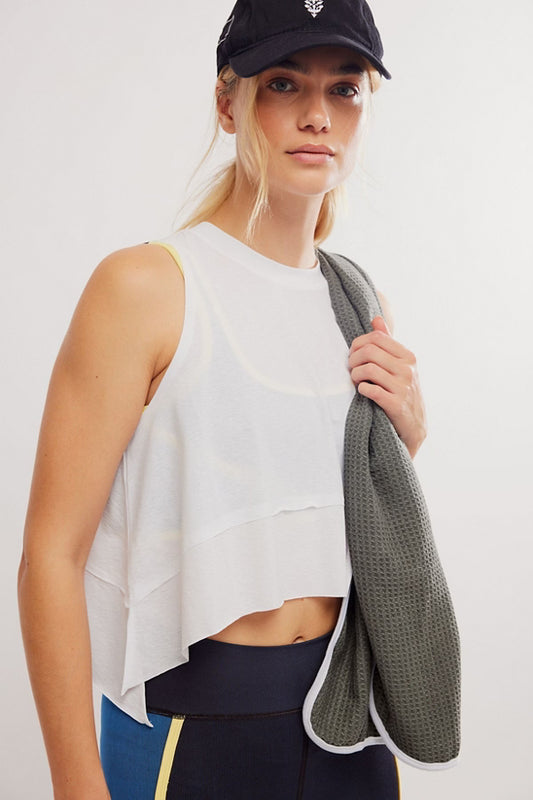 Woman holding a gray towel, wearing a white sleeveless top and black cap on a light background