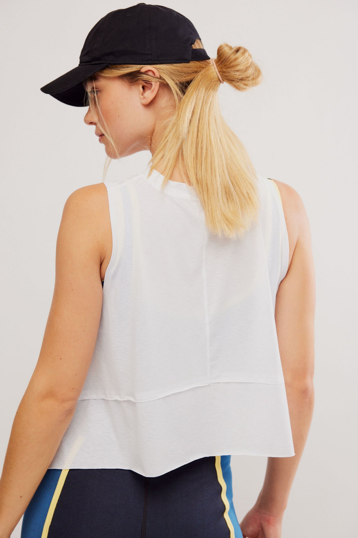 Woman wearing a white sleeveless top and black cap on a plain background
