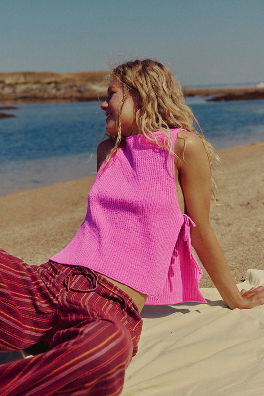 Woman in pink top and red striped pants sitting on a beach.