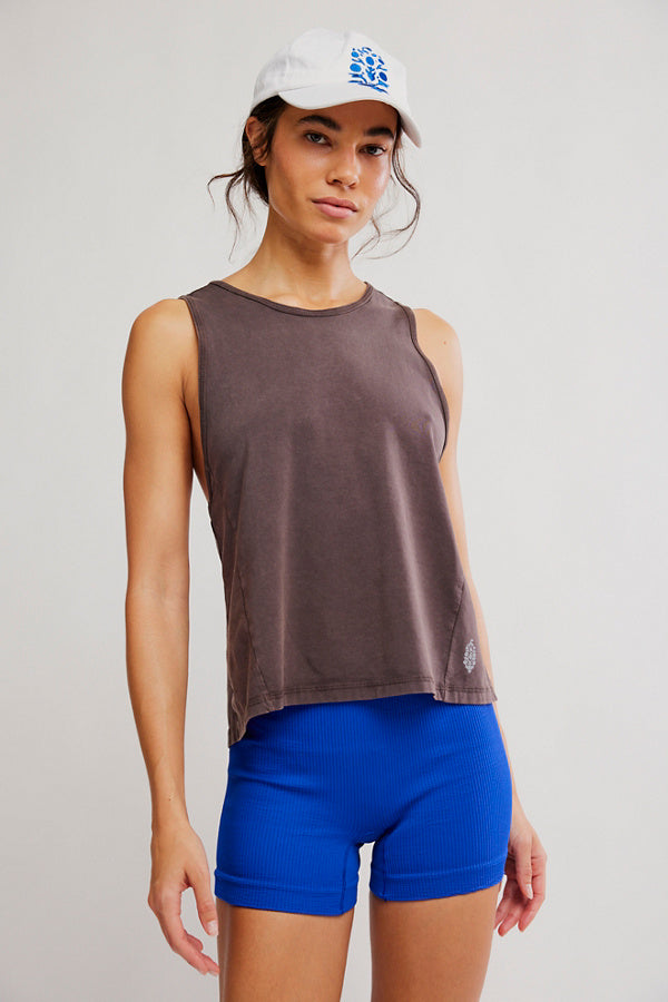 Woman wearing a brown sleeveless top and blue shorts with a white cap featuring a logo.