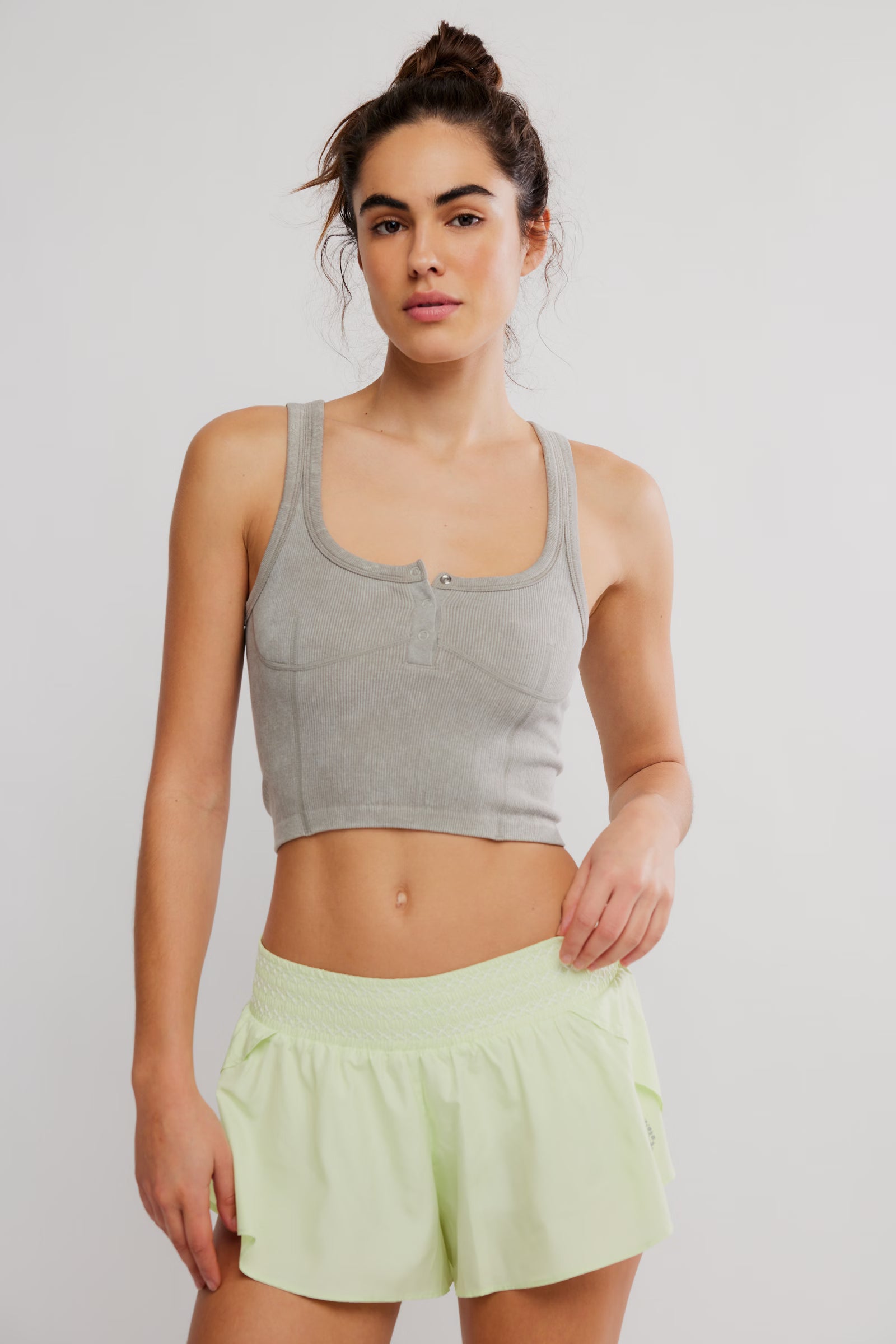 Woman wearing a gray crop top and light green shorts on a plain background