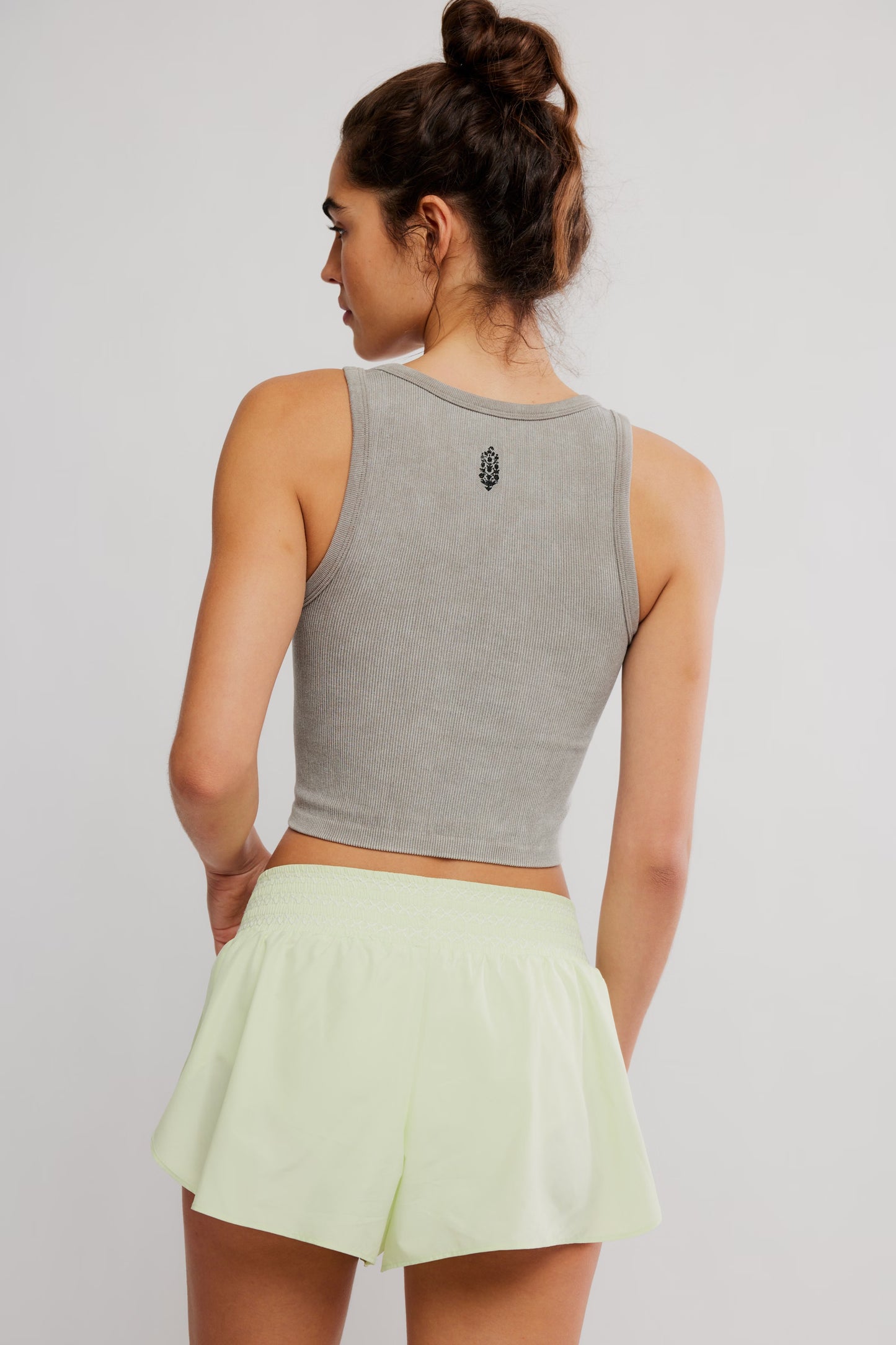 Woman wearing a gray tank top and light green shorts on a plain background