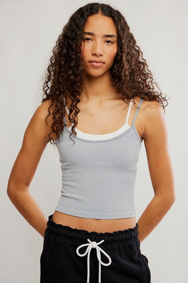 Woman wearing a gray tank top and black pants with white drawstrings on a plain background