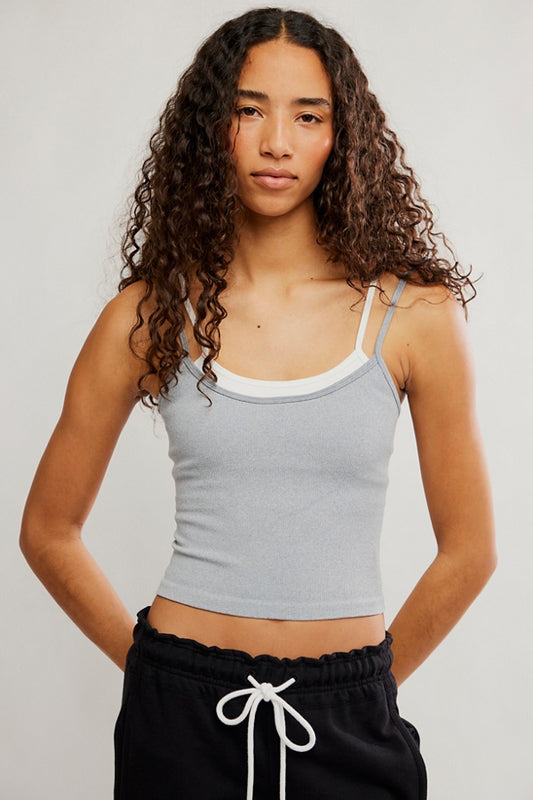Woman wearing a gray tank top and black pants with white drawstrings on a plain background