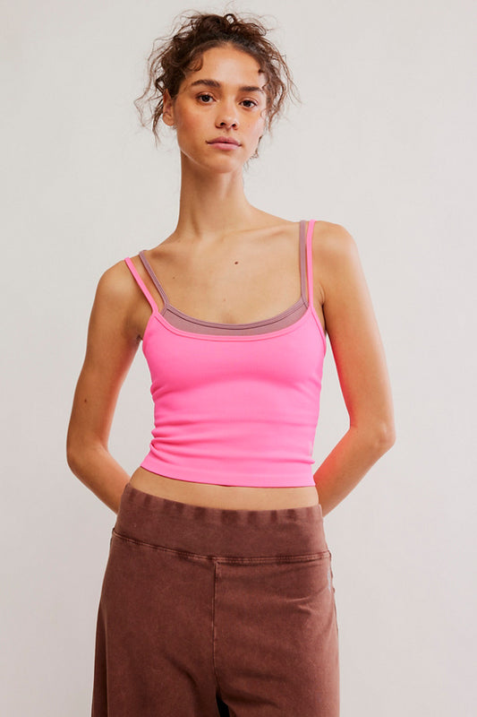 Woman wearing a pink tank top and brown pants against a plain background