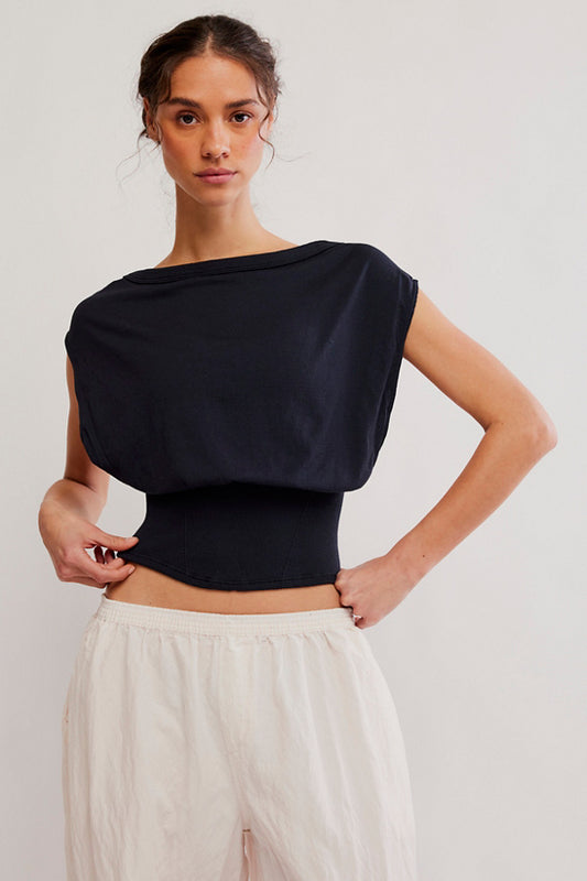 Woman wearing a black top and white pants against a plain background