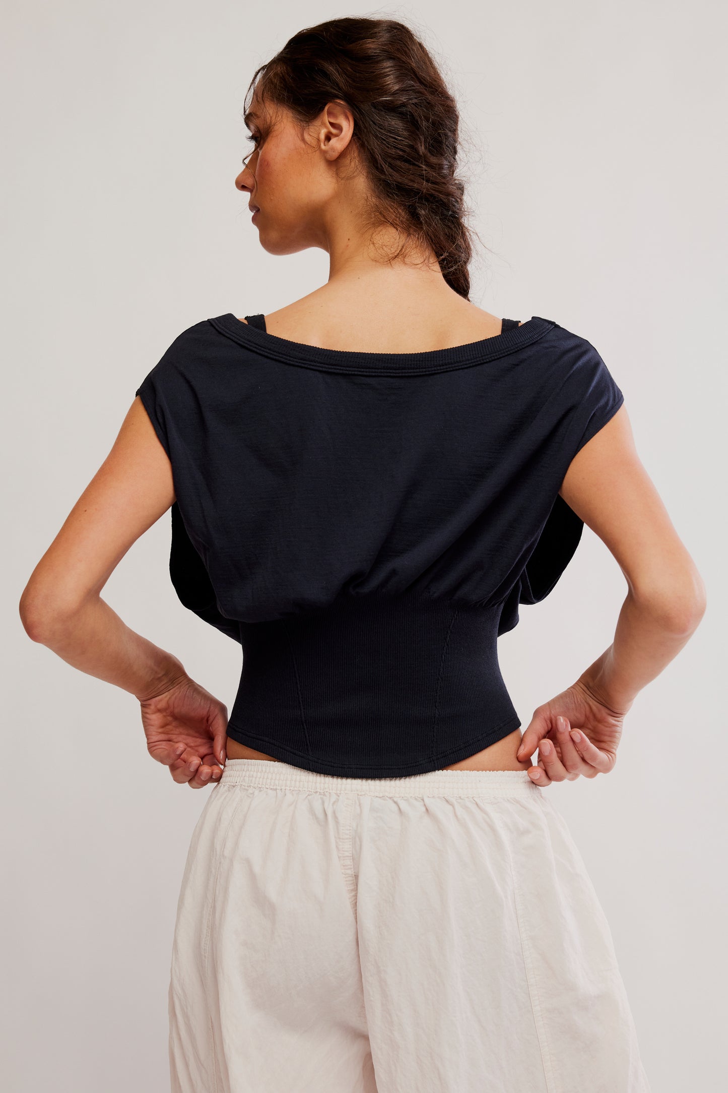 Woman wearing a black top and white pants against a plain background