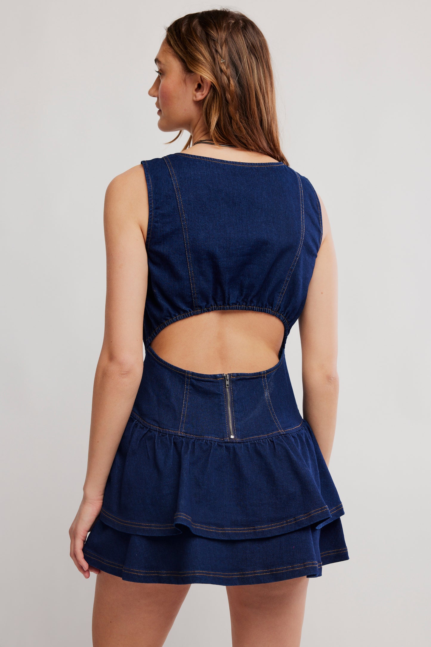 Woman wearing a navy blue denim dress with cut-out back on a light gray background
