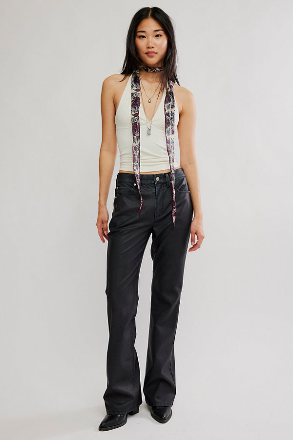 Woman wearing a white tank top, black pants, and a patterned scarf with a neutral background