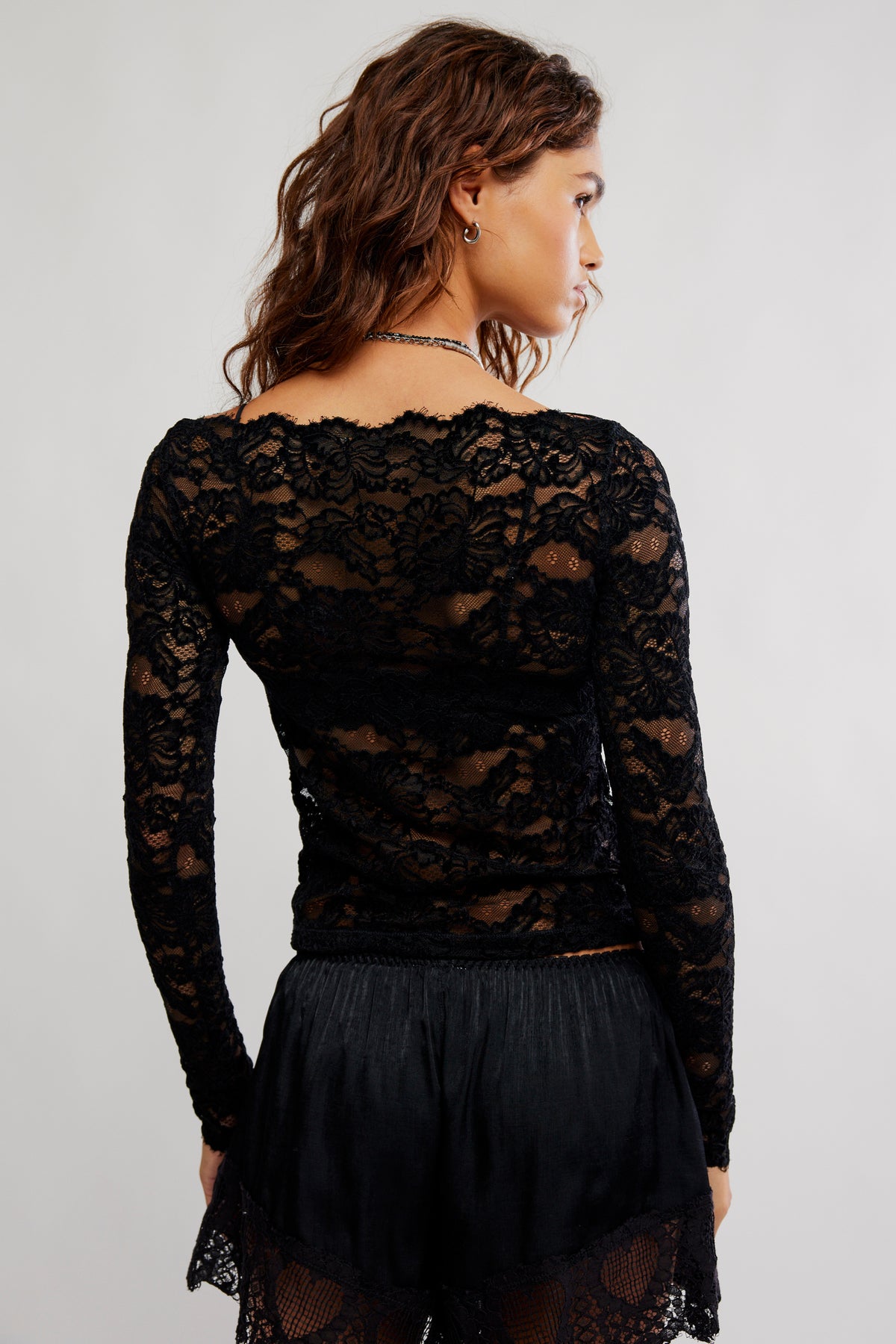 Woman wearing a black lace long-sleeve top and skirt on a plain background