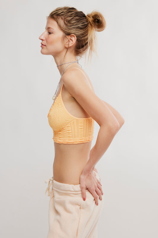 Woman wearing a yellow sports bra and beige pants on a light gray background