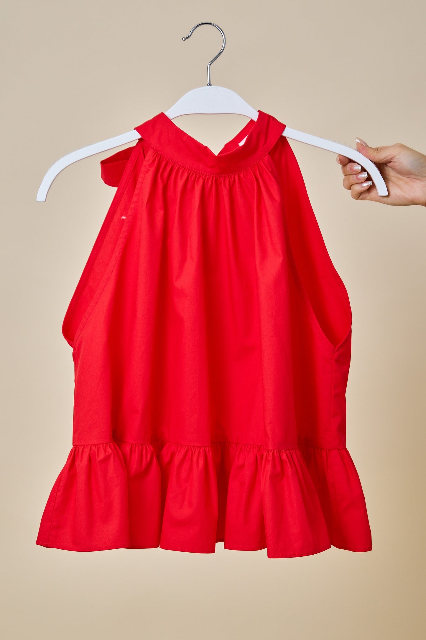 Red halter top on a hanger against a beige background