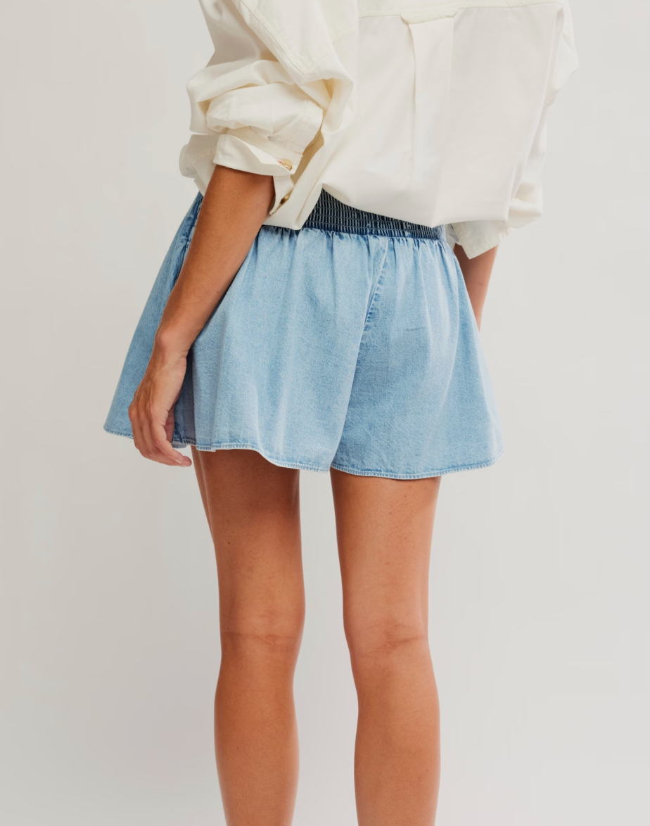 Person wearing a light blue denim skirt and white blouse on a plain background