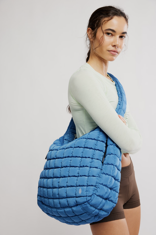Woman carrying a blue quilted bag on a plain background
