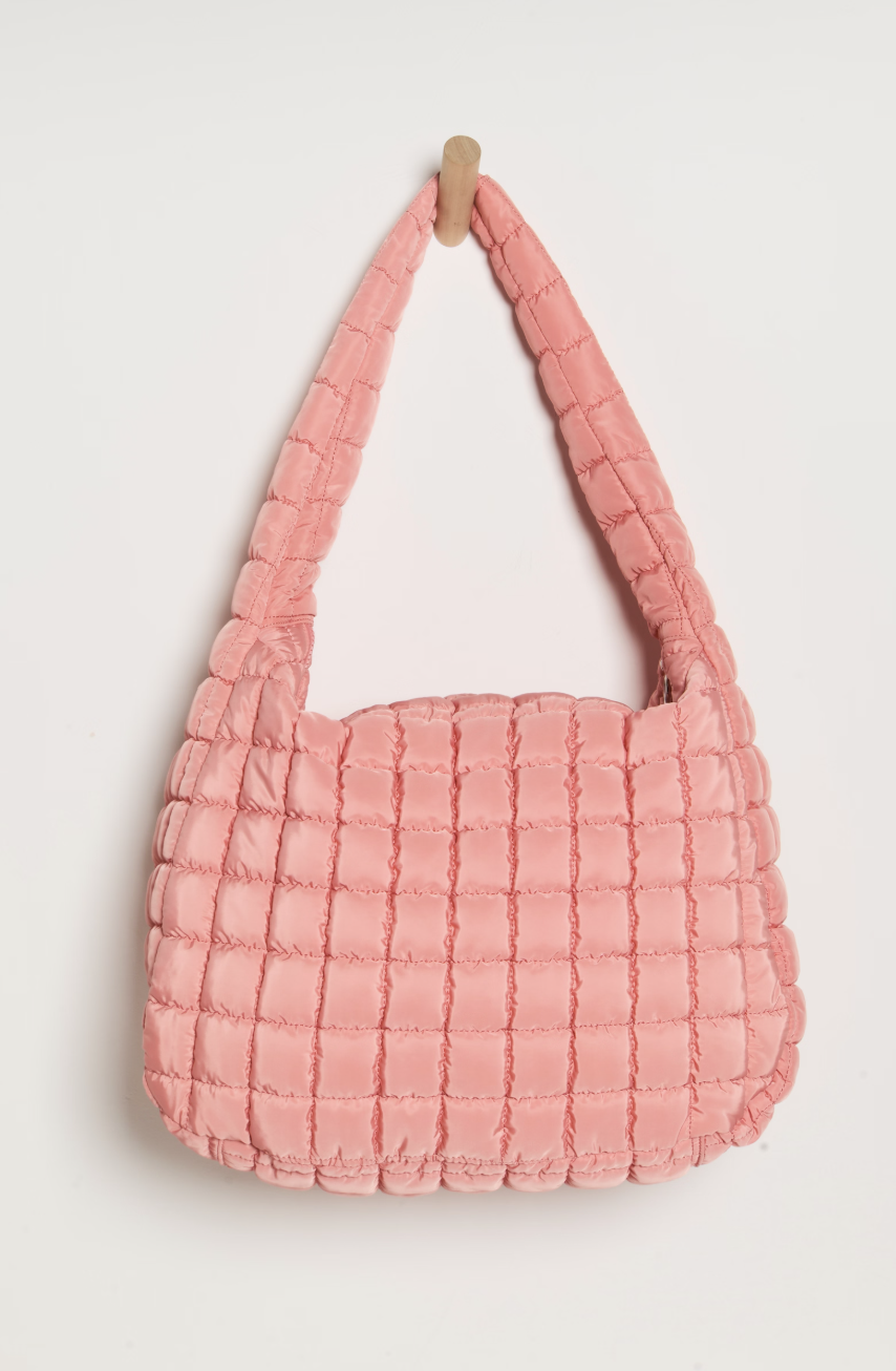 A pink quilted shoulder bag with a thick strap, hanging from a small wooden peg against a plain off-white background.