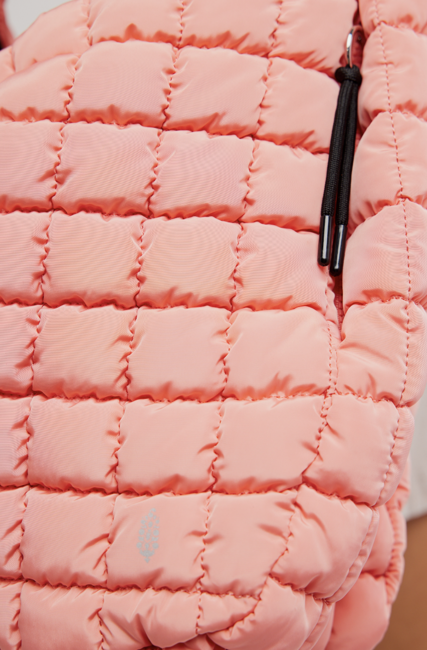 Close-up of a quilted puffer jacket in a soft peach-pink color, showing the stitched grid pattern and a black zipper pull.
