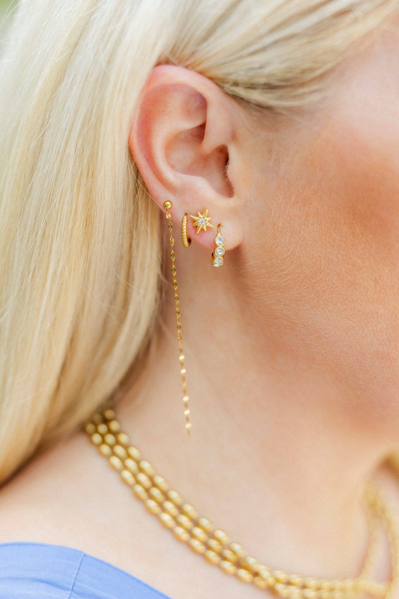 Close-up of a person wearing gold earrings and a necklace with a blurred background