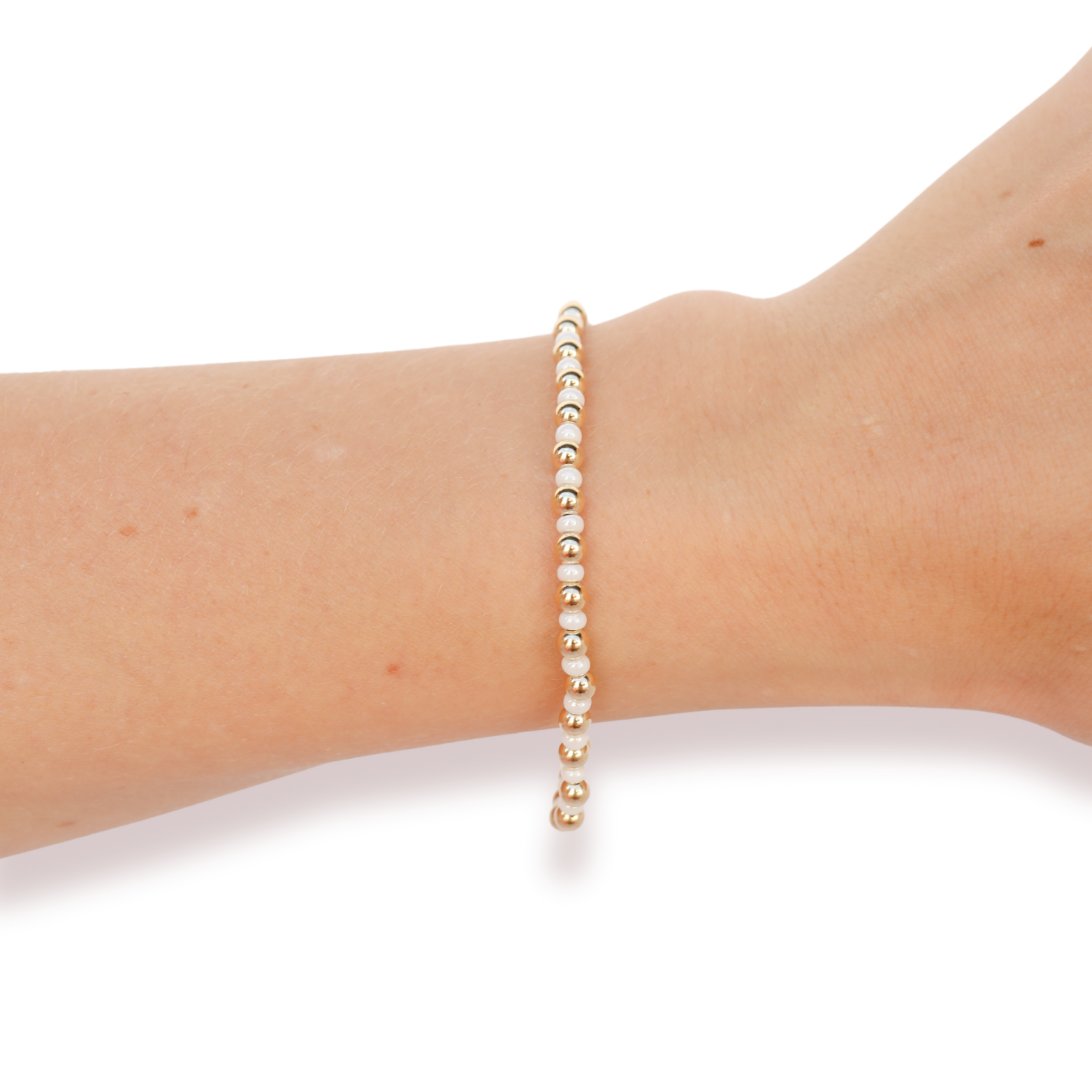 A delicate beaded bracelet with small white pearls and gold spacer beads, shown worn on a person's wrist against a plain white background.