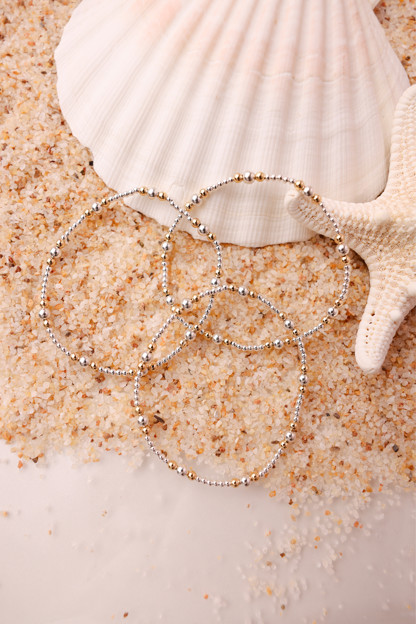 Three beaded bracelets on sand with a shell and starfish in the background