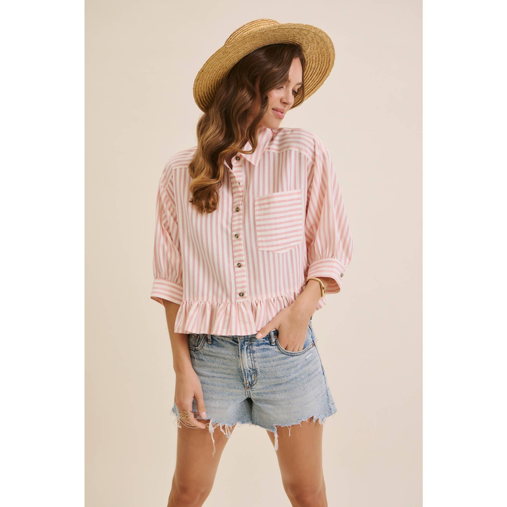 Woman wearing a striped shirt, denim shorts, and a straw hat on a beige background
