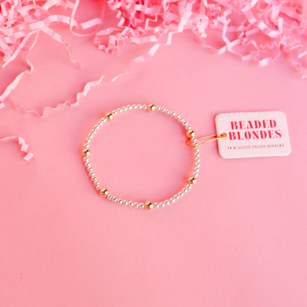 Bracelet with 'Beaded Blondes' tag on a pink background