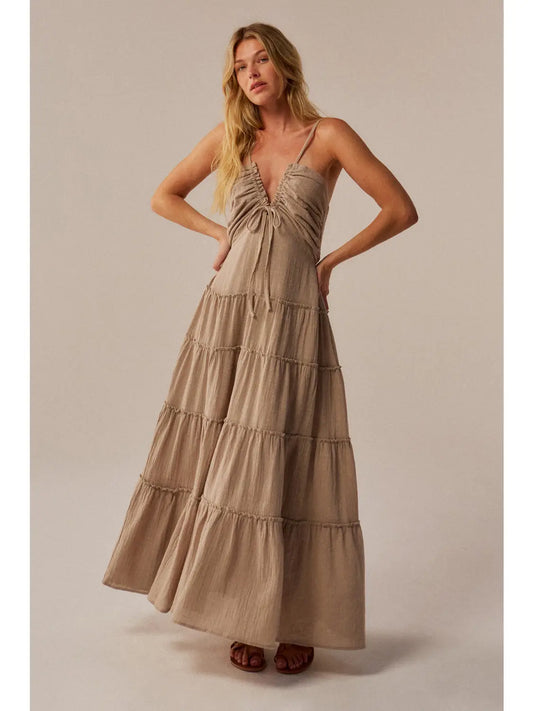 Woman wearing a beige tiered dress against a plain background