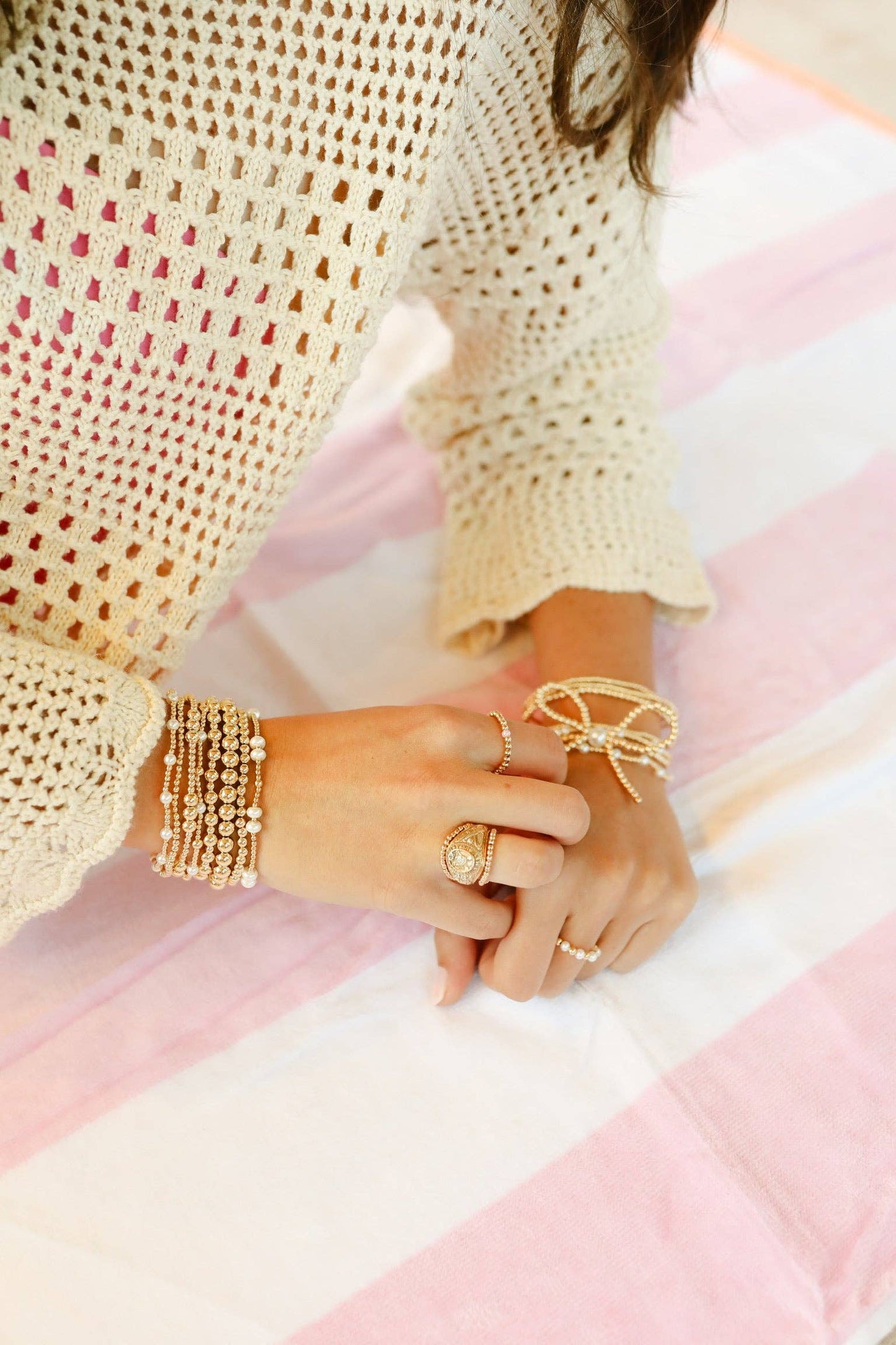Close-up of hands wearing gold jewelry on a pink and white striped fabric background