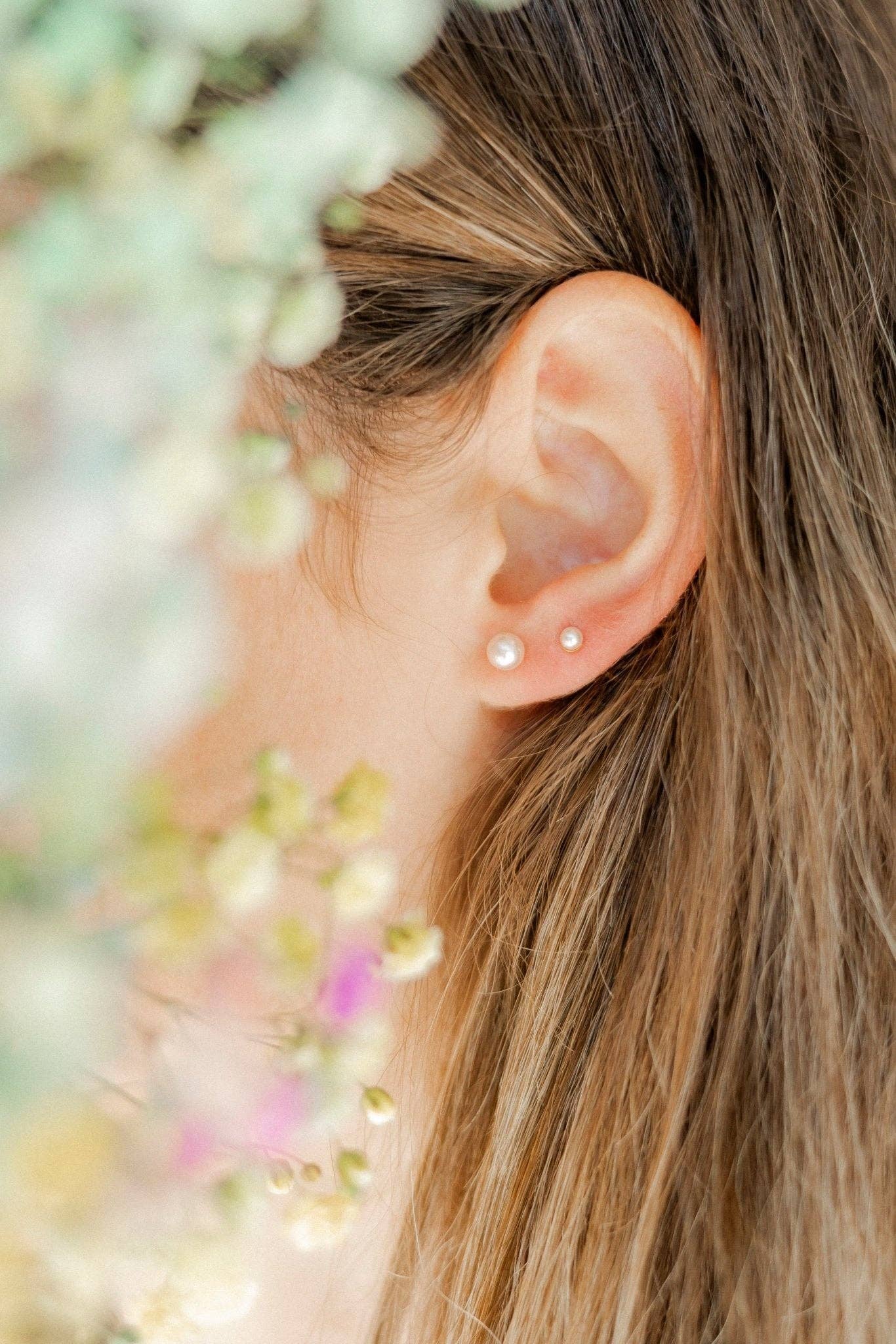 Close-up of an ear with pearl earrings against a blurred floral background