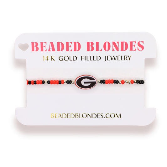 A beaded bracelet displayed on a white branded card. The bracelet features red, black, and blonde beads with a Georgia Bulldogs logo charm in the center.