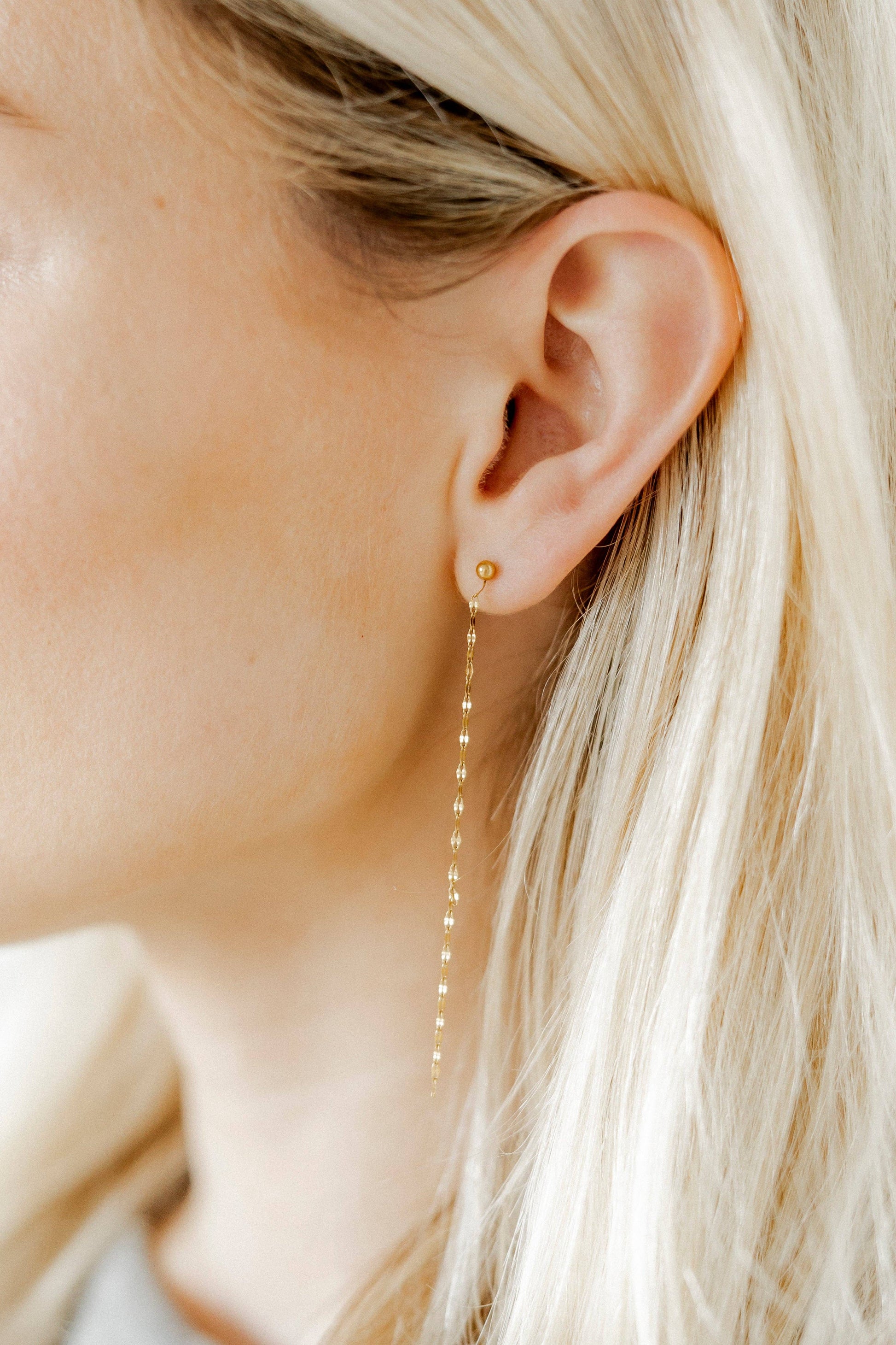 Close-up of a person wearing a gold earring with a chain