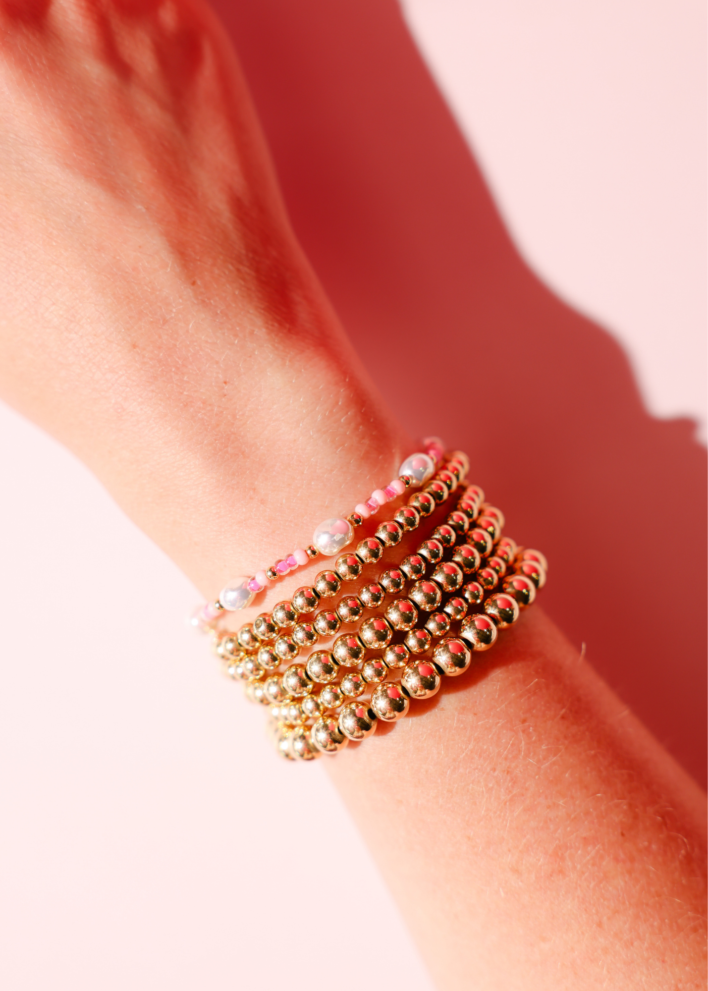 Stack of gold beaded bracelets on a wrist with a soft pink background