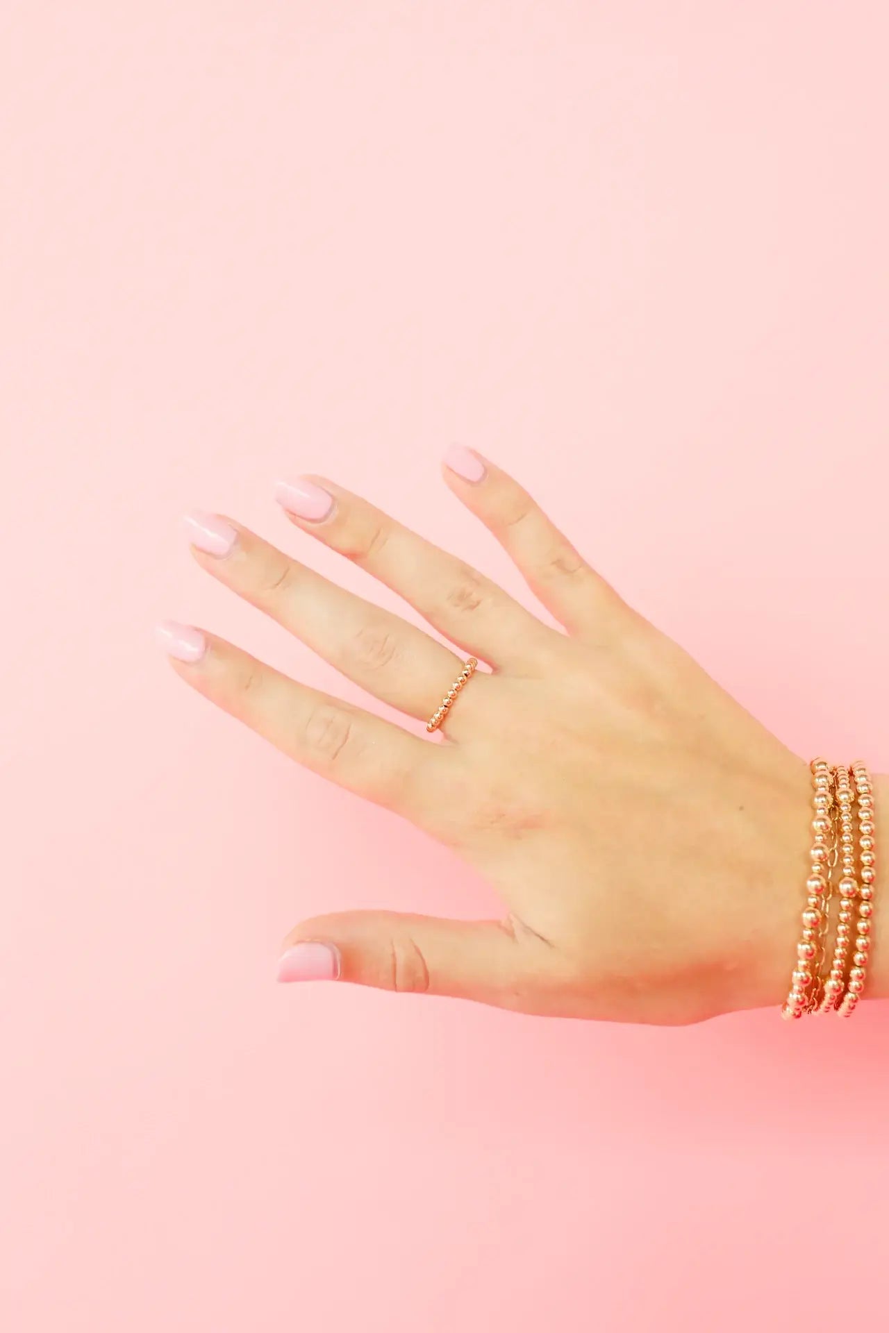 Hand wearing multiple rings and bracelets on a pink background