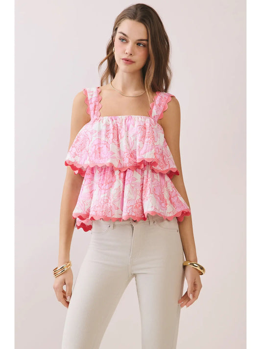 Woman wearing a pink and white ruffled top with white pants on a light background