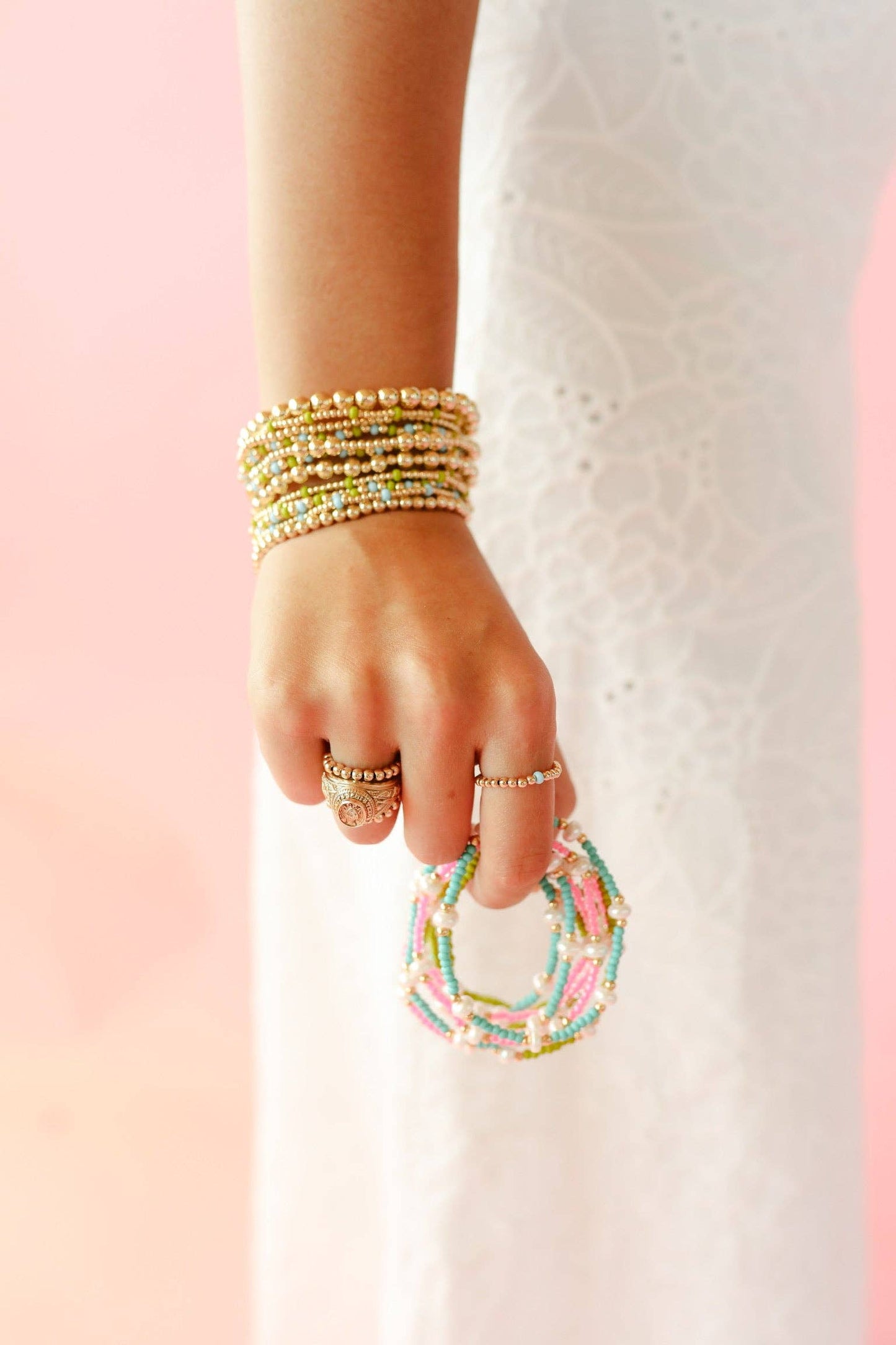 Hand wearing multiple beaded bracelets on a pink and white background