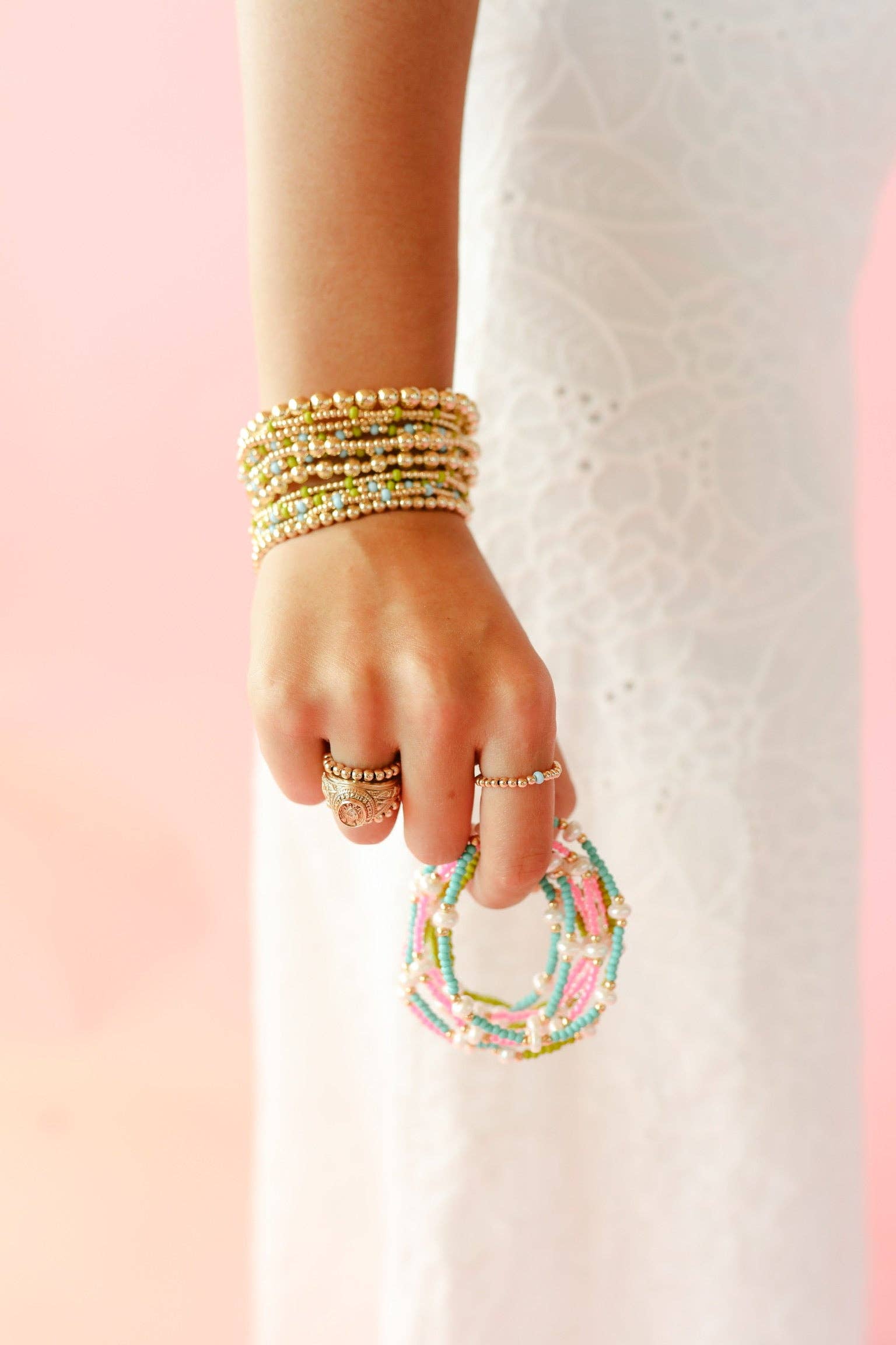 Hand wearing multiple beaded bracelets on a pink and white background