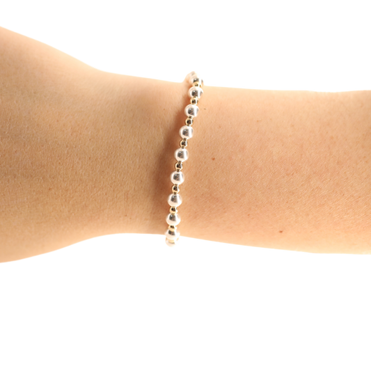 A delicate silver beaded bracelet worn on a person's wrist, shown against a plain white background.