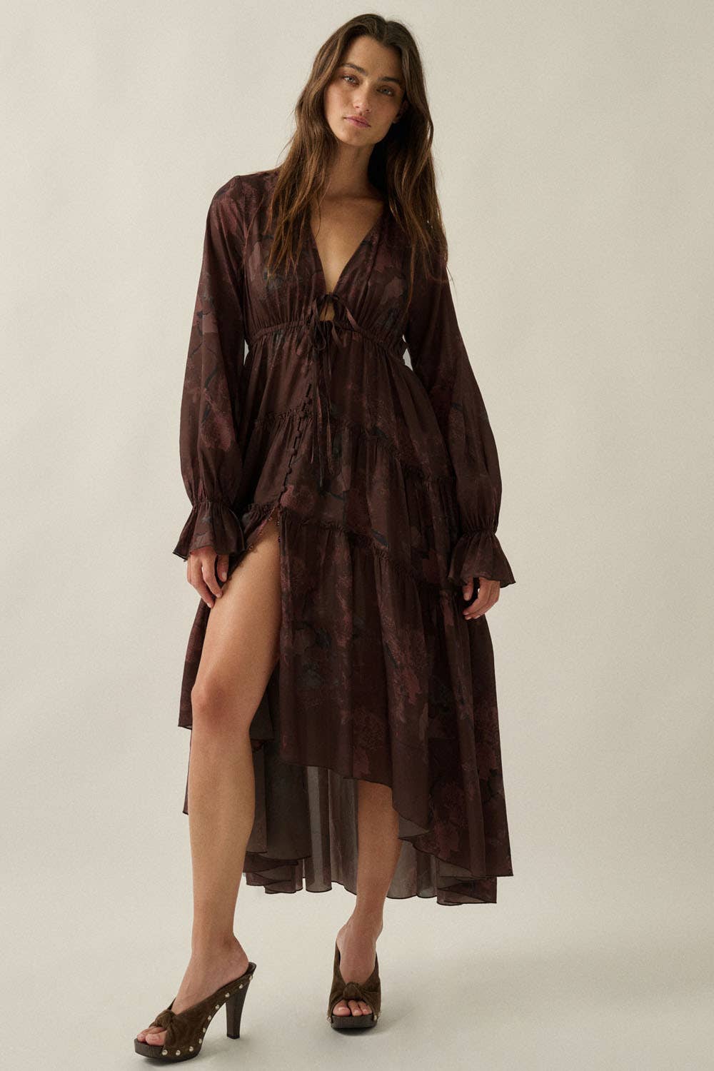 Woman wearing a long brown dress with a slit on a plain background