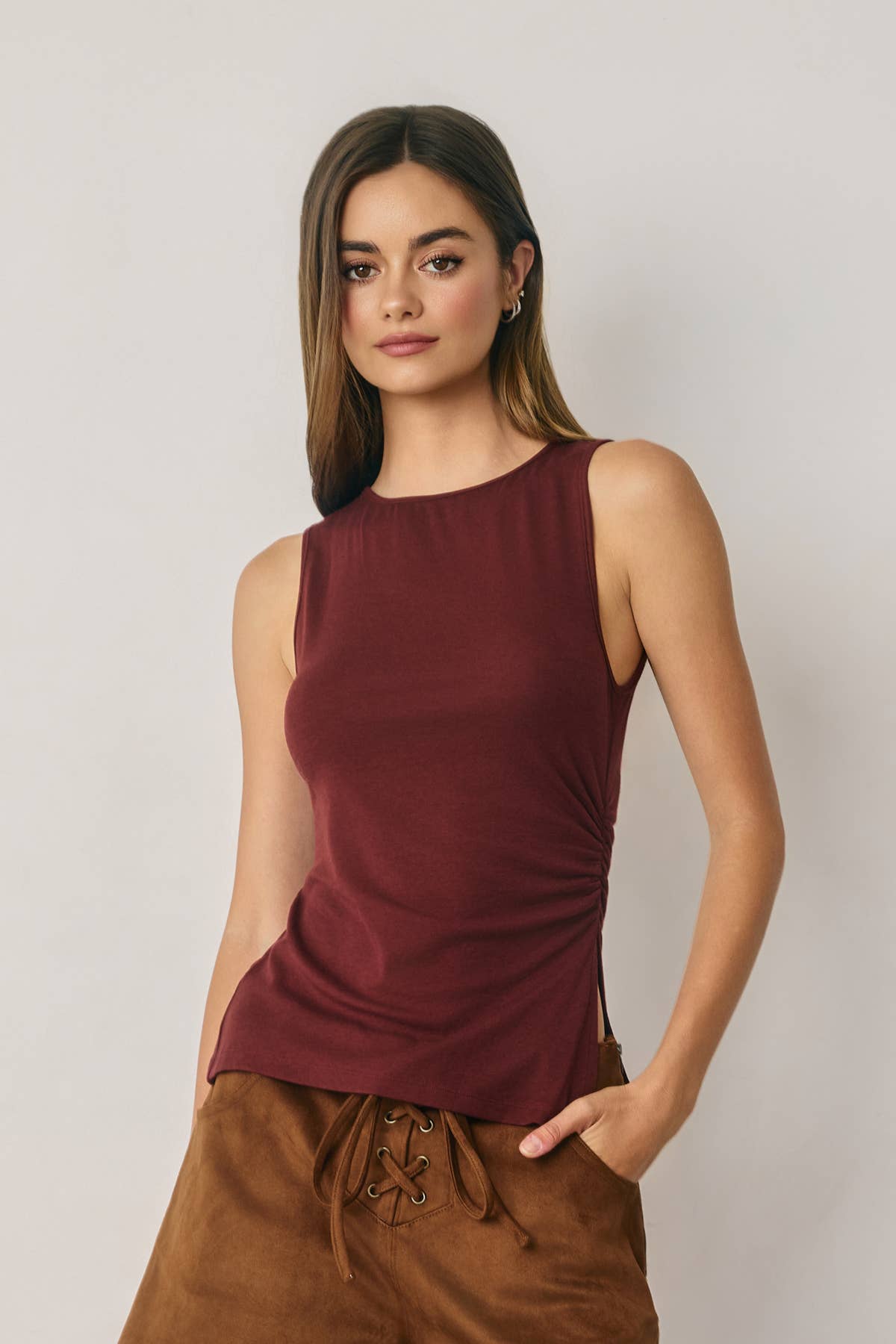 Woman wearing a burgundy sleeveless top and brown pants against a plain background