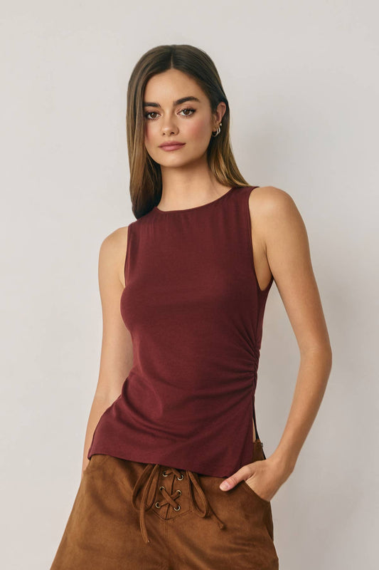 Woman wearing a burgundy sleeveless top and brown pants against a plain background