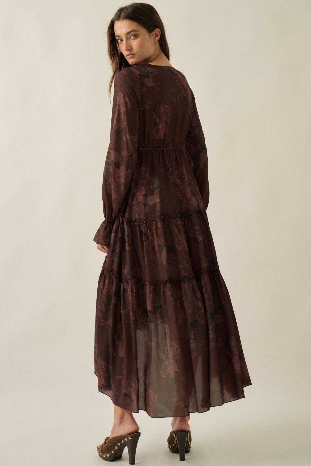 Woman wearing a long, dark brown dress with a subtle pattern on a beige background