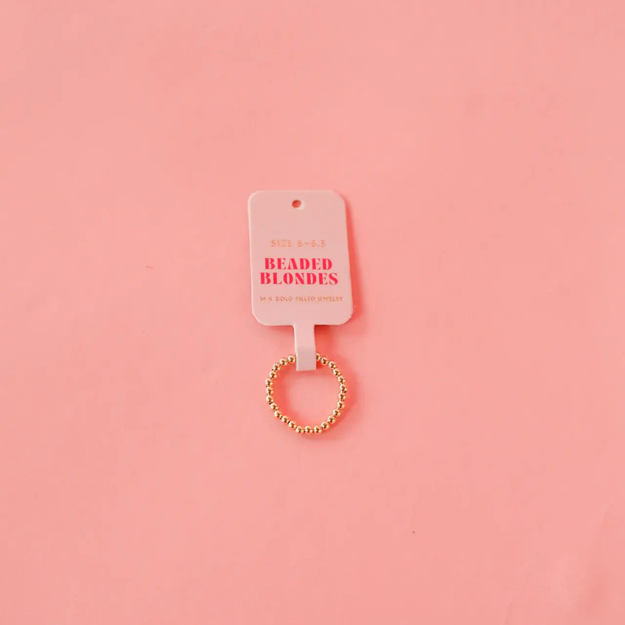 Gold beaded hair tie on a pink background with 'Beaded Blondes' label.