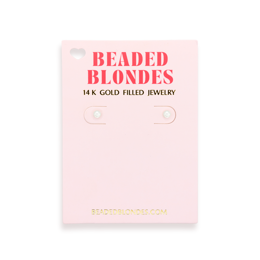 A pair of small round stud earrings displayed on a light pink backing card. The card reads 'BEADED BLONDES' in coral-red letters and '14 K GOLD FILLED JEWELRY' in black, with the website BEADEDBLONDES.