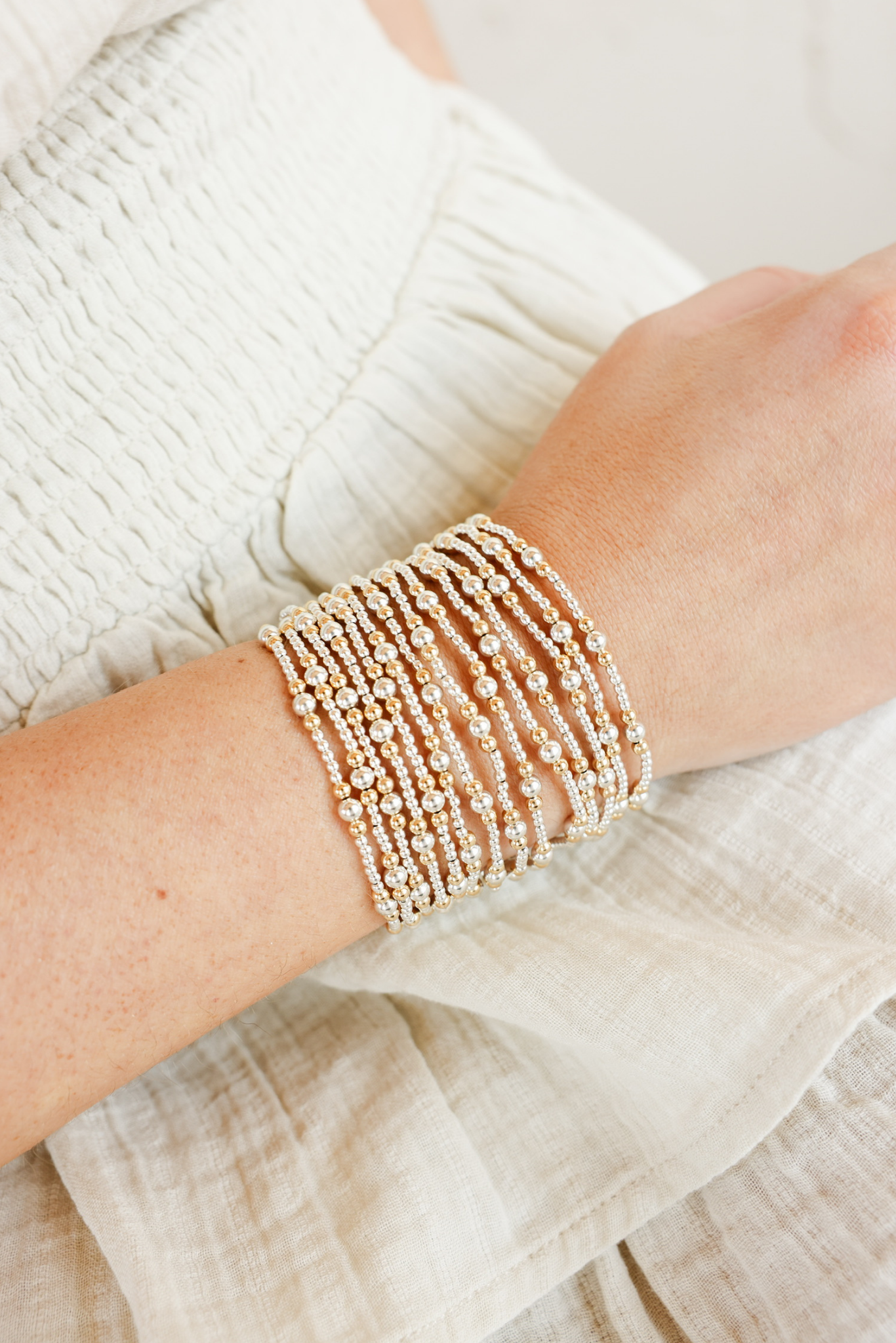 Close-up of a wrist wearing multiple pearl bracelets on a light background