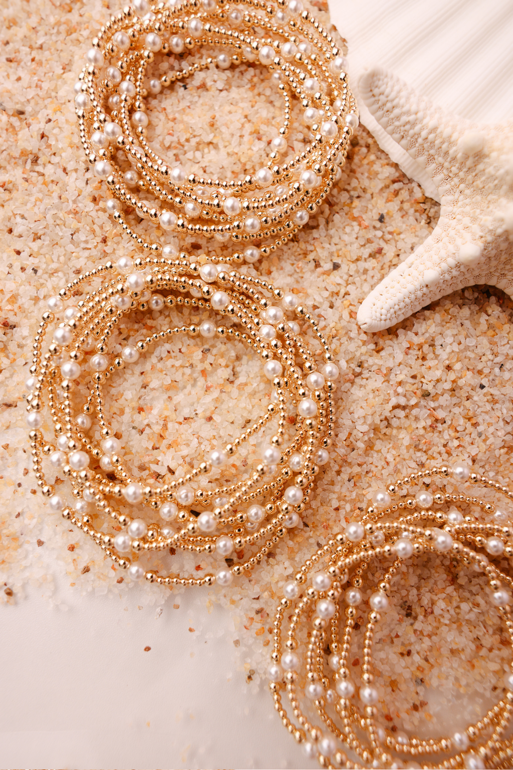 Gold bracelets with pearls on a sandy surface with a starfish.