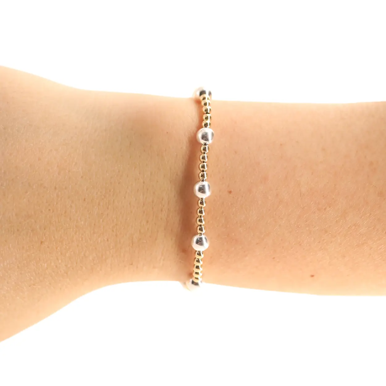 A delicate gold beaded bracelet with five polished silver ball accents, shown worn on a person's wrist against a plain white background.
