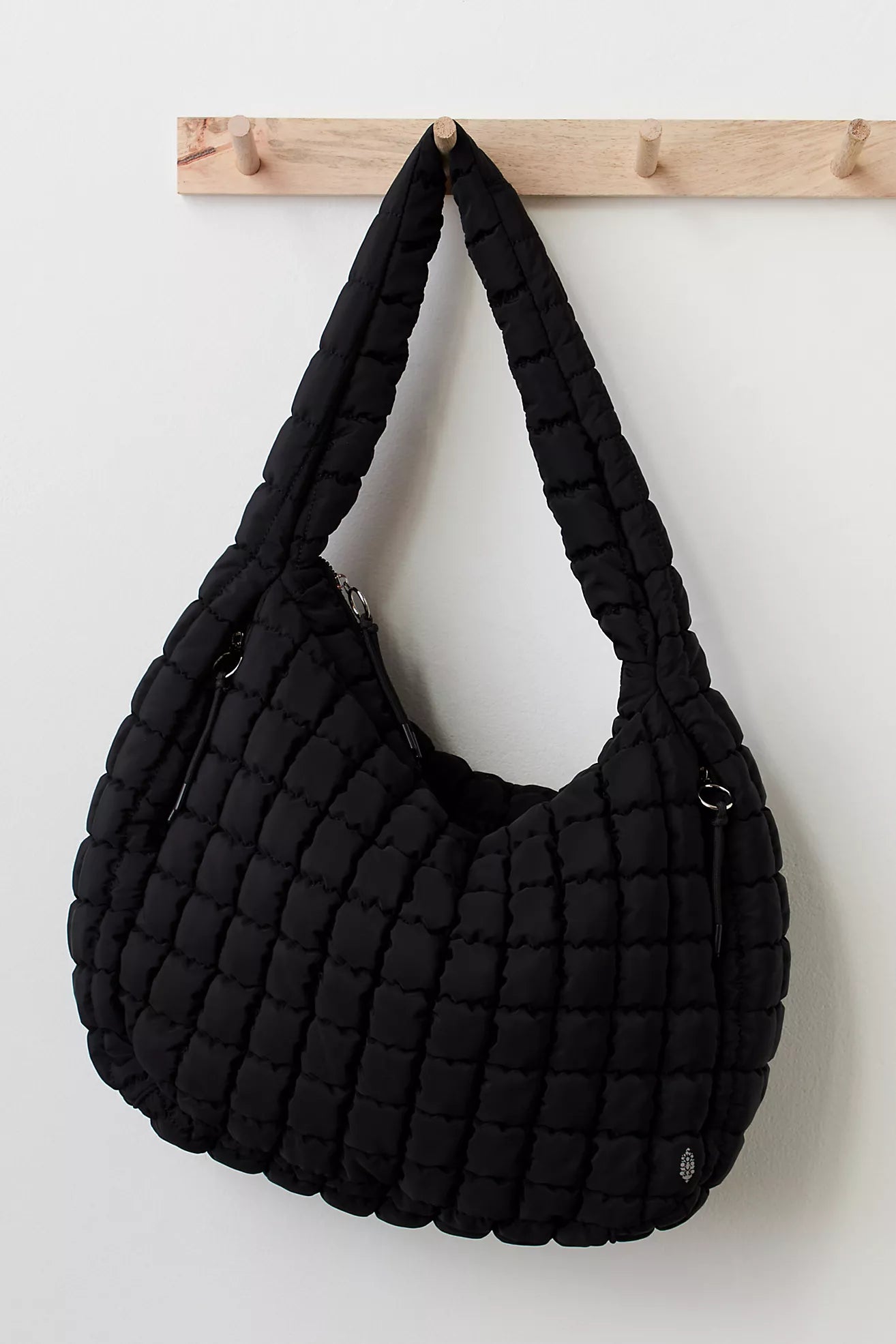 Black quilted handbag hanging on a wooden rack against a white background