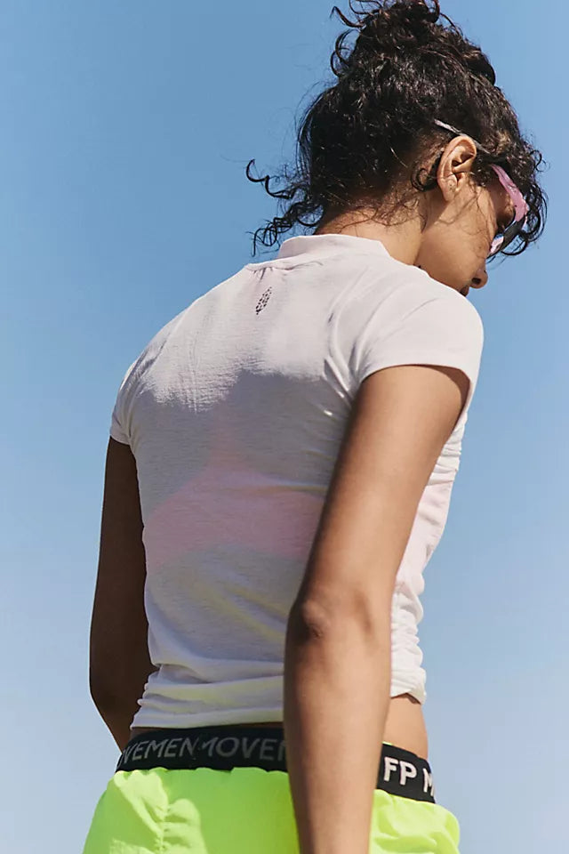 A woman shown from behind wearing a fitted white short-sleeve athletic top and neon yellow shorts, photographed outdoors against a clear blue sky. The waistband of the shorts shows the brand name FPN.