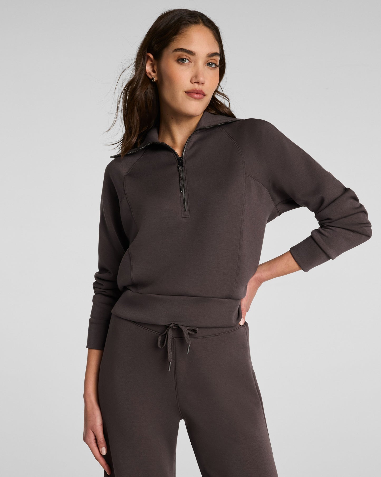 Woman wearing a dark brown tracksuit on a light gray background