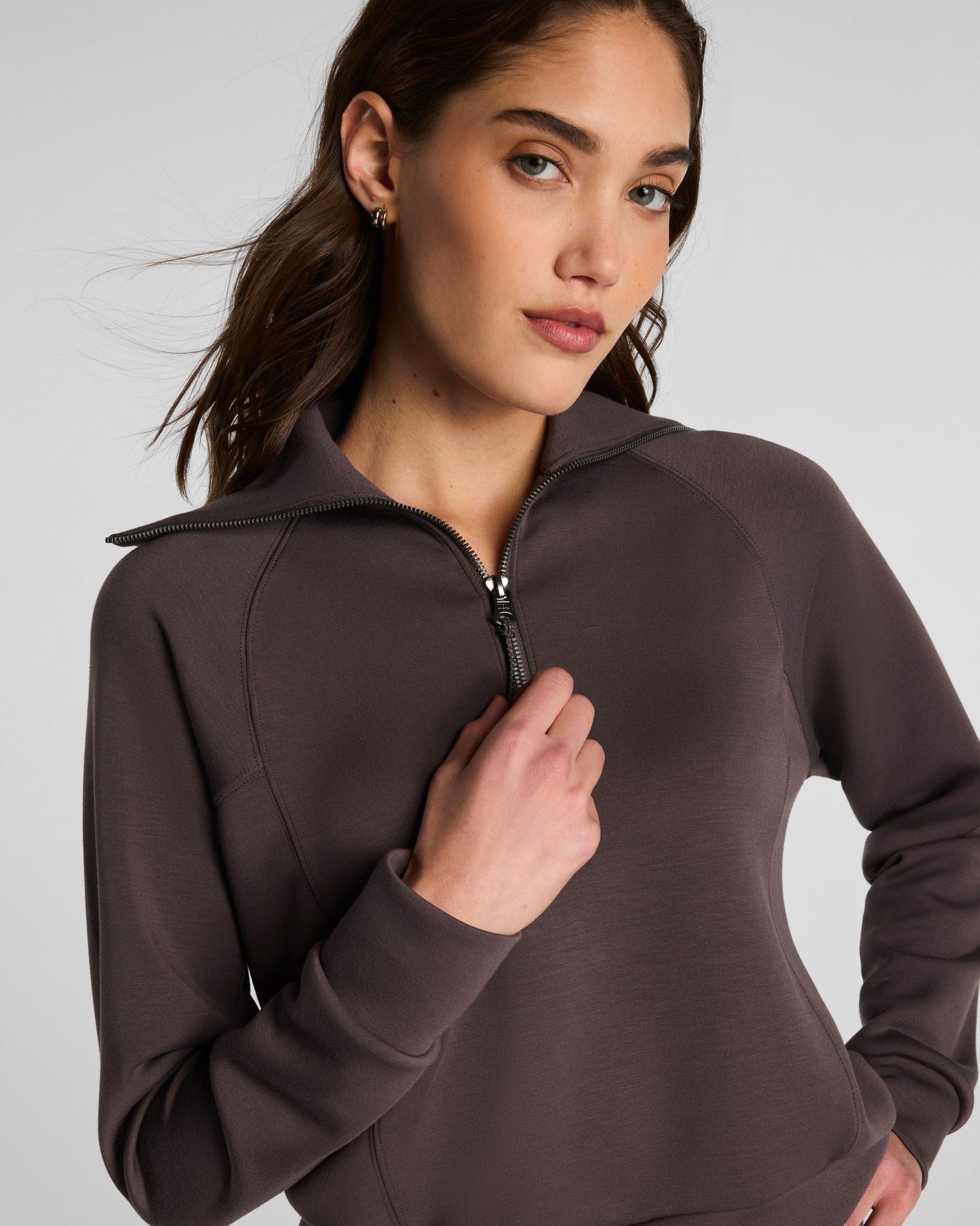 Woman wearing a brown zip-up sweatshirt against a light gray background